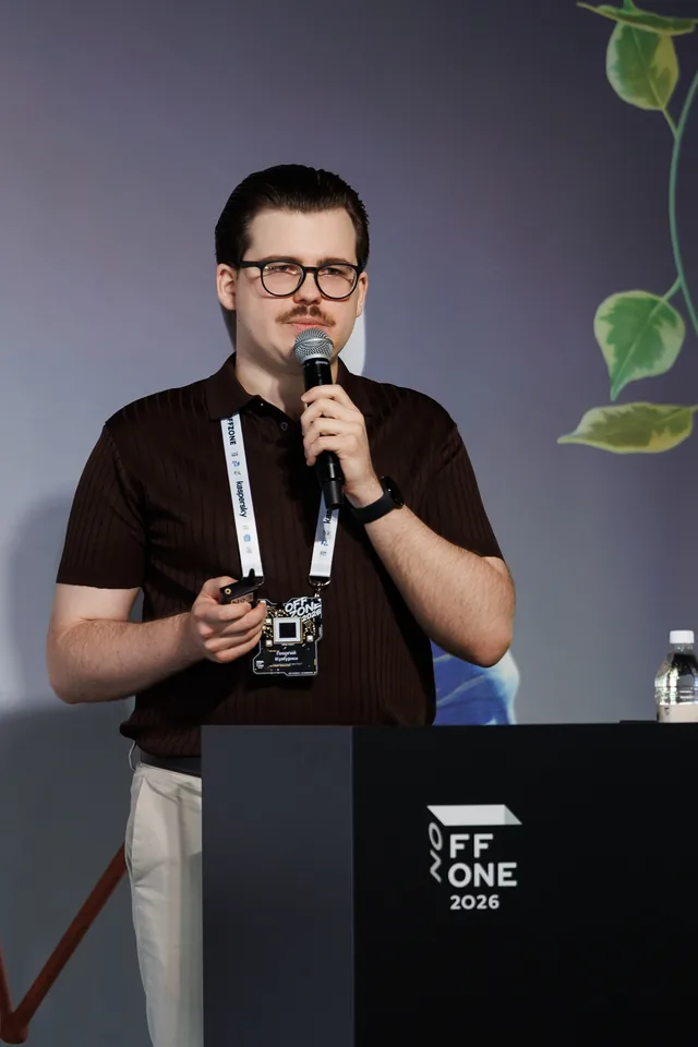 Georgii Kumurzhi holding a microphone and presentation remote at the OFFZONE 2026 lectern